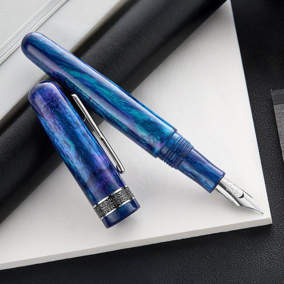 A close-up shot of a Conklin 1898 fountain pen with a swirled blue and turquoise resin body. The pen has silver trim, a decorative band around the base of the cap, and a 